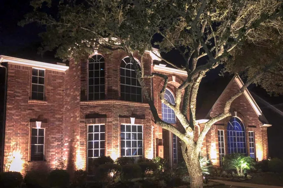 Brick elevation and a mature live oak lit together on a River Oaks property