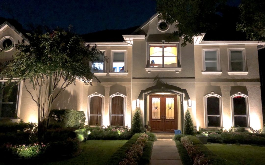 A large 2 story home with a free in front is lit up by Houston residential lighting