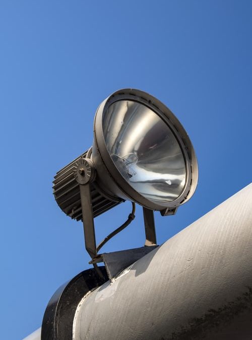 Outdoor LED lighting fixture perched on the top of a thick horizontal pole against blue sky