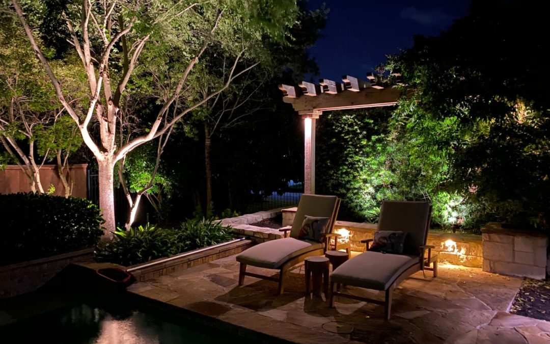 Backyard lights illuminate lounge chairs next to a pool