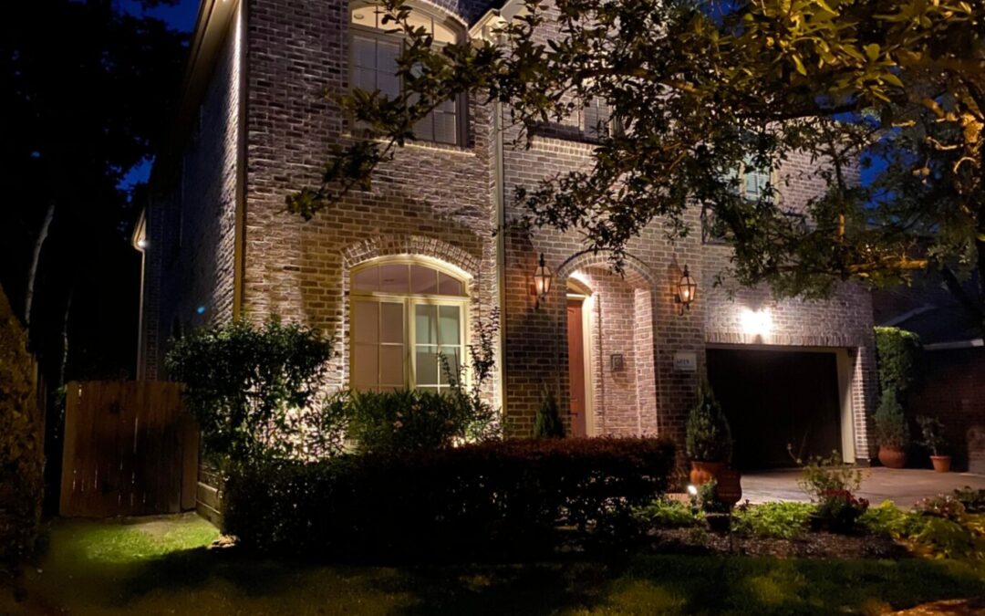 A brick house at night with a tree in front illuminated by fall landscape lighting