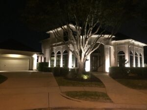 A white columned house lit up at night by Fall landscape lighting