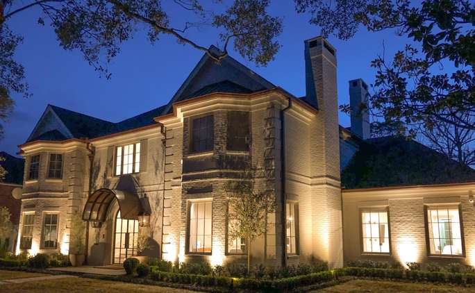The West University Place Texas Hearth Home has big windows and a door arch that are lit up at dusk