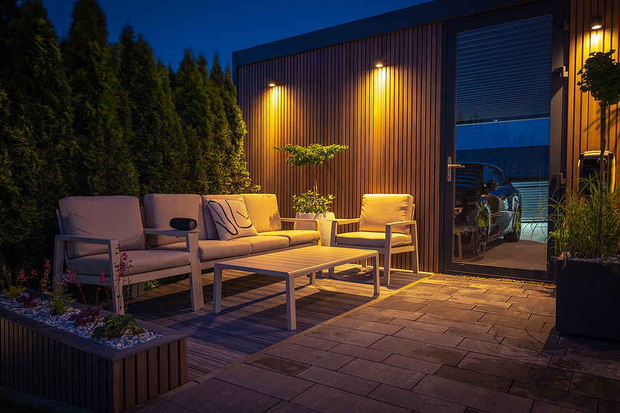 Lounge and Dining Area at Modern Residential Backyard Decorated with Outdoor Lights, Plants, Garden Table and Chairs. Cozy Summer Evening. Oudoor lighting can