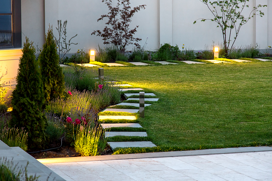 A well-lit backyard with a marble walkway and flowerbed, highlighting the right outdoor lighting for safety and style.