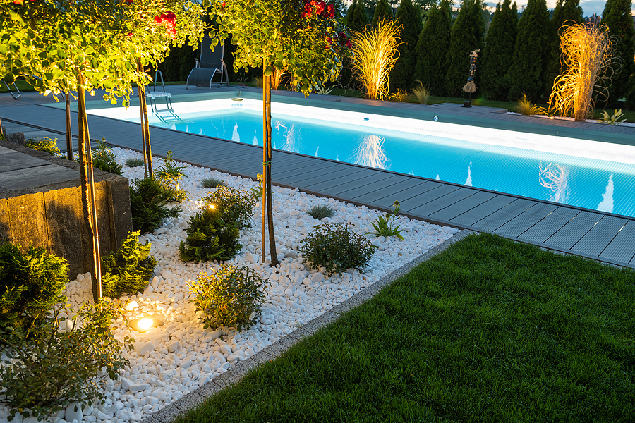 Modern residential pool illuminated by LED lights at night, surrounded by a landscaped patio and palm trees.